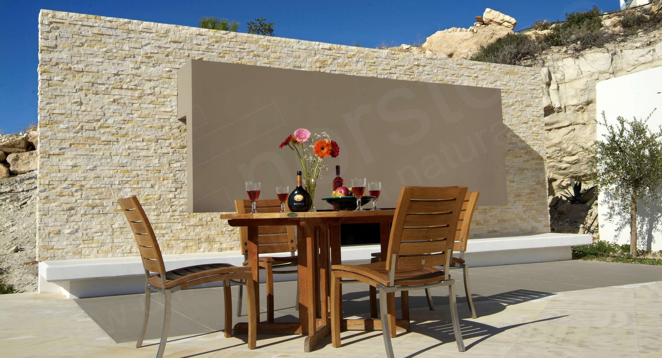 Norstone Ivory Rock Panels on an outdoor feature wall surrounding an open air patio with dining chairs in Cyprus